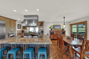 Kitchen featuring wall chimney exhaust hood, recessed lighting, wood finished floors, glass insert cabinets, and appliances with stainless steel finishes