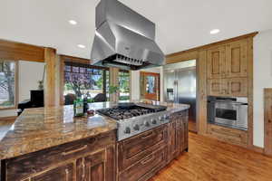 Kitchen with exhaust hood, stainless steel appliances, light stone countertops, light wood-type flooring, and recessed lighting