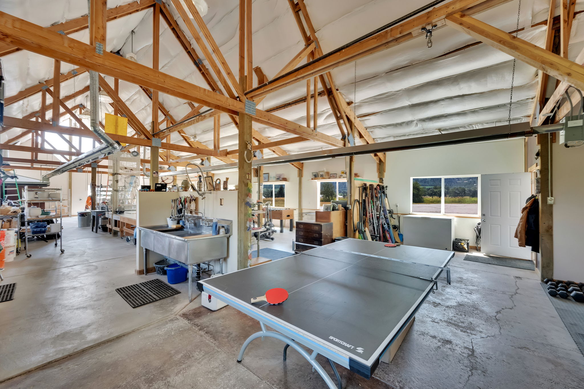 Game room featuring unfinished concrete flooring, high vaulted ceiling, and a workshop area