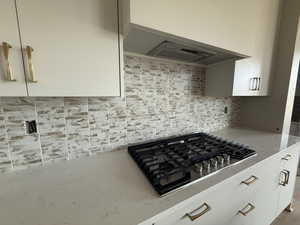 Kitchen with stainless steel gas cooktop, tasteful backsplash, white cabinets, range hood, and light stone counters