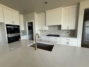 Kitchen featuring light stone countertops, decorative backsplash, double oven, and gas stovetop