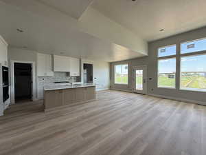 Kitchen with open floor plan, light countertops, light wood-style floors, an island with sink, and tasteful backsplash