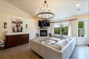 Living room with wood finished floors, a chandelier, a fireplace, lofted ceiling, and recessed lighting