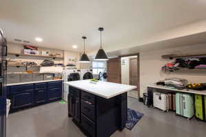 Kitchen with washing machine and dryer, finished concrete flooring, light countertops, a center island, and blue cabinets