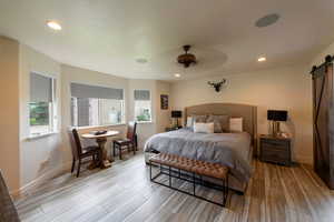 Bedroom with a barn door, light wood-type flooring, recessed lighting, and a ceiling fan