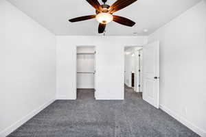Unfurnished bedroom featuring dark colored carpet, a walk in closet, and ceiling fan
