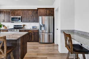 Kitchen featuring stainless steel appliances, light wood-style flooring, dark brown cabinetry, and light stone counters