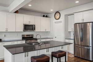 Kitchen with stainless steel appliances, dark countertops, a kitchen breakfast bar, white cabinets, and recessed lighting