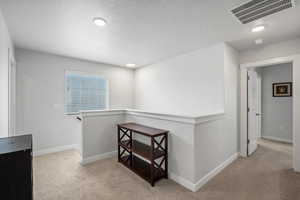 Hall featuring an upstairs landing, carpet, and a textured ceiling