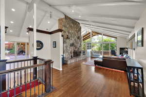 Living room featuring beam ceiling, wood finished floors, healthy amount of natural light, high vaulted ceiling, and a stone fireplace