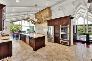 Kitchen with beamed ceiling, ceiling fan, appliances with stainless steel finishes, high vaulted ceiling, and light stone counters