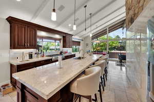 Kitchen with an island with sink, light stone counters, and pendant lighting