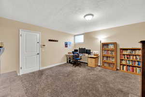 Carpeted home office featuring a textured ceiling and baseboards