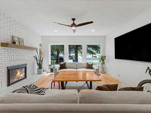 Living area featuring engineered hardwood finished floors, ceiling fan, a brick fireplace, recessed lighting, and large windows