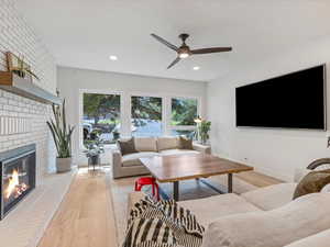 Living room with light flooring, a fireplace, a ceiling fan, and recessed lighting