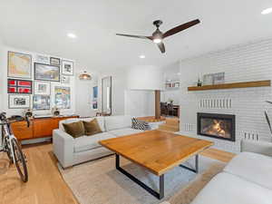 Living room with a brick (gas) fireplace, light wood flooring, ceiling fan, and recessed lighting