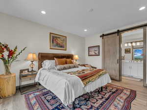 Bedroom with a barn door, light wood-type flooring, recessed lighting, and connected bathroom