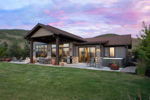 Back of house with a hot tub, a patio area, a yard, and a shingled roof