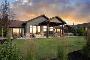Rear view of house featuring a patio, an outdoor living space, a lawn, and stone siding