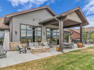 Rear view of property with a hot tub, a patio area, an outdoor living space with a fire pit, a yard, and stone siding