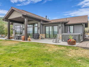Back of property with a hot tub, a patio, a shingled roof, and a yard