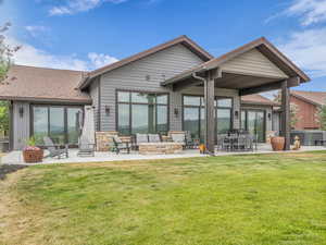 Back of house with a patio area, roof with shingles, a yard, stone siding, and an outdoor living space