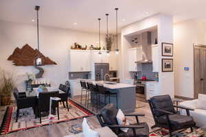 Kitchen with stainless steel appliances, wall chimney range hood, a breakfast bar area, light countertops, and an island with sink