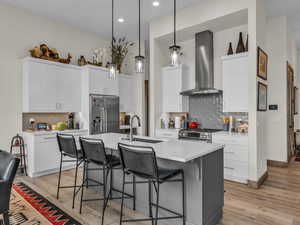 Kitchen with a kitchen breakfast bar, backsplash, wall chimney range hood, light countertops, and recessed lighting