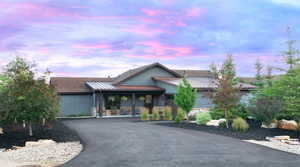 View of front facade with a standing seam roof, a metal roof, asphalt driveway, a porch, and stone siding