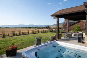 Fenced backyard with a mountain view, a rural view, a hot tub, and a patio