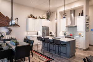 Kitchen featuring a breakfast bar, wall chimney range hood, light countertops, stainless steel appliances, and light wood-style flooring