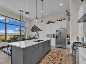 Kitchen with appliances with stainless steel finishes, white cabinetry, a center island with sink, light wood finished floors, and a chandelier