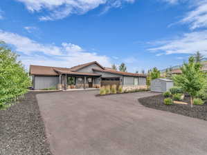 View of front of home featuring stone siding, a storage unit, driveway, and a porch
