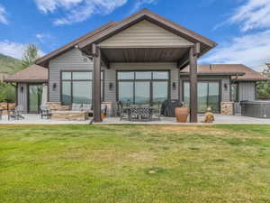 Rear view of house featuring stone siding, a patio, a shingled roof, and a lawn