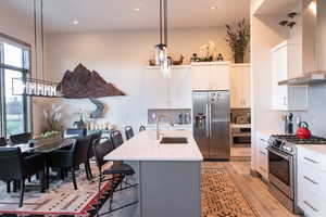 Kitchen with appliances with stainless steel finishes, wall chimney range hood, tasteful backsplash, hanging light fixtures, and a breakfast bar area