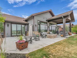 Back of house with a patio area, a shingled roof, an outdoor living space with a fire pit, a yard, and stone siding