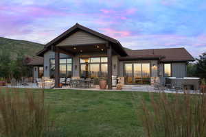 Back of property with a patio, a yard, roof with shingles, and stone siding