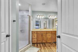 Master bath with a shower stall, wood finished floors, and double vanity