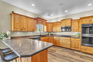 Kitchen with dark countertops, stainless steel appliances, a peninsula, a breakfast bar, and recessed lighting
