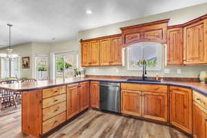 Kitchen with stainless steel dishwasher, a chandelier, light wood-style floors, decorative light fixtures, and a peninsula