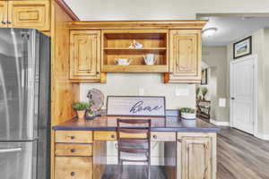 Kitchen with freestanding refrigerator, built in study area, dark countertops, wood finished floors, and open shelves