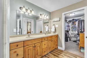 Full bath featuring double vanity, a walk in closet, and wood finished floors