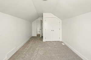 Bonus room with light colored carpet and vaulted ceiling