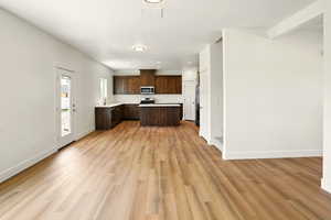 Kitchen featuring light countertops, dark brown cabinets, open floor plan, light wood-style floors, and recessed lighting