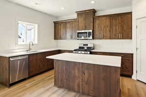 Kitchen featuring appliances with stainless steel finishes, light wood-type flooring, a kitchen island, light countertops, and recessed lighting