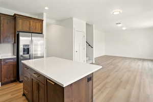 Kitchen with stainless steel fridge with ice dispenser, light wood-style floors, light countertops, a center island, and recessed lighting