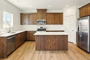 Kitchen with stainless steel appliances, light wood-type flooring, a kitchen island, light countertops, and recessed lighting