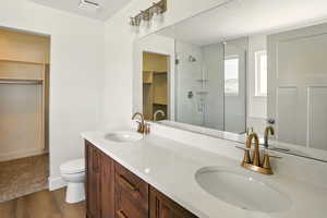 Full bathroom featuring a stall shower, wood finished floors, double vanity, and a walk in closet