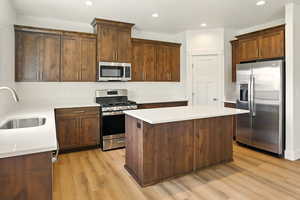 Kitchen featuring appliances with stainless steel finishes, light wood finished floors, a center island, recessed lighting, and light countertops