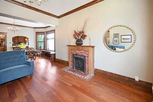 Living area featuring a chandelier, a fireplace, wood finished floors, and crown molding